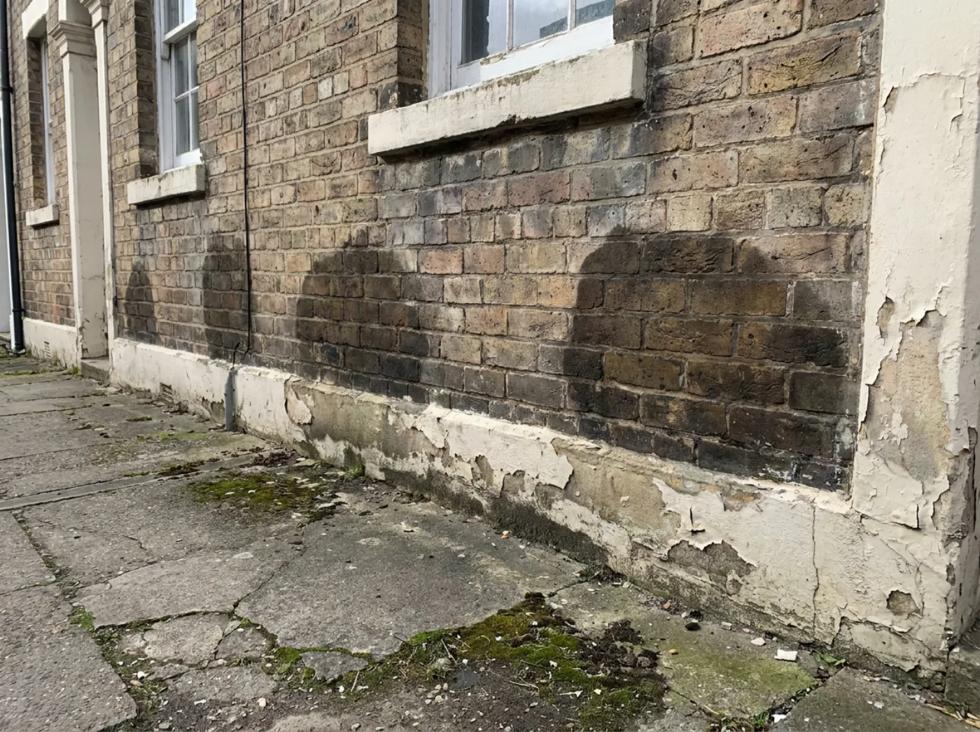 Fachada con manchas de humedad y deterioro en la base del muro